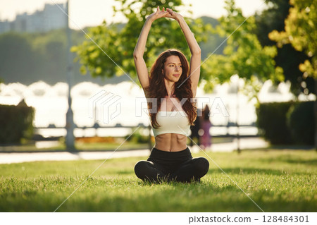 Yoga practice. Beautiful young woman in sportive clothes is in the park at sunny daytime Yoga practice. Beautiful young woman in sportive clothes is in the park at sunny daytime 128484301