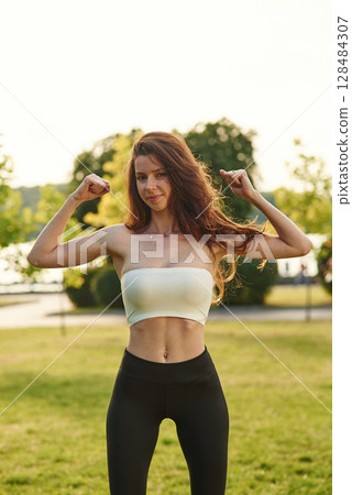 Beautiful young woman in sportive clothes is in the park at sunny daytime 128484307