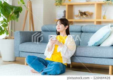 在房間裡操作智慧型手機的年輕女子 在房間裡操作智慧型手機的年輕女子 128484426