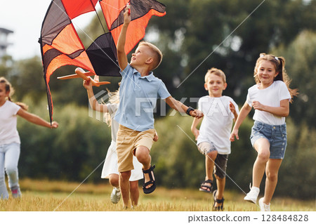 Group of kids are running and playing with kite on green field 128484828