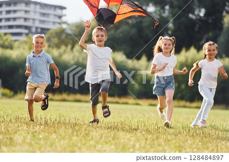 Running together. Group of kids are running and playing with kite on green field 128484897
