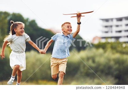 Front view. Boy and girl are playing with toy plane on the green field 128484948