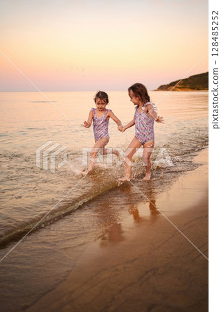 Sisters laughing and playing together on a serene beach at sunset 128485252