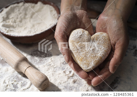 Baking concept. Caucasian female hands holding heart shaped dough. 128485361