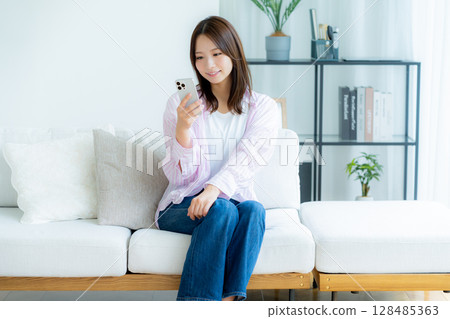 A young woman operating a smartphone in a room A young woman operating a smartphone in a room 128485363