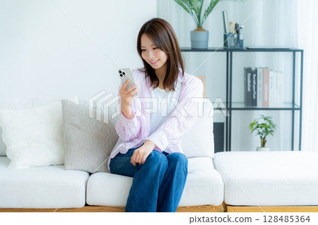 A young woman operating a smartphone in a room 128485364