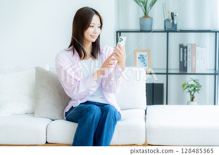 A young woman operating a smartphone in a room A young woman operating a smartphone in a room 128485365
