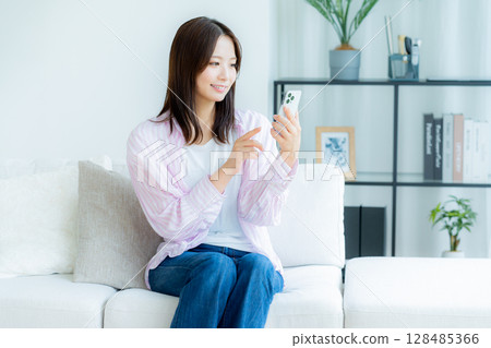 A young woman operating a smartphone in a room A young woman operating a smartphone in a room 128485366