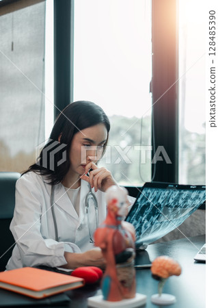 A focused female doctor examines an X-ray in a contemporary medical office, highlighting professional healthcare and diagnosis. A focused female doctor examines an X-ray in a contemporary medical office, highlighting professional healthcare and diagnosis. 128485390