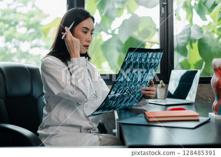 Female doctor examines X-ray in a bright office, surrounded by greenery, showcasing a blend of technology and nature. Female doctor examines X-ray in a bright office, surrounded by greenery, showcasing a blend of technology and nature. 128485391