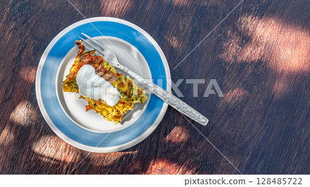 Delicious vegetable casserole topped with sour cream rests on a plate outdoors, showcasing vibrant colors in natural light Delicious vegetable casserole topped with sour cream rests on a plate outdoors, showcasing vibrant colors in natural light 128485722