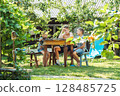 Three brothers are having lunch at a round wooden table in a lush garden, surrounded by greenery and sunlight 128485725