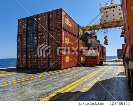 Loading cargo containers onto ship at busy port under clear skies 128486563