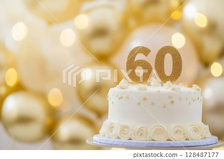 60th birthday cake, adorned with gold accents. Birthday party. Blurred light festive background. Golden balloons. Sixty years or sixtieth anniversary. Celebration cake with golden candles. Numbers 60 128487177