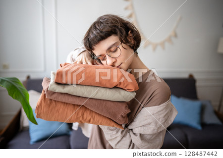 Calm young woman embracing clean laundry with joy, fresh nice scent. Linens conditioner aroma 128487442