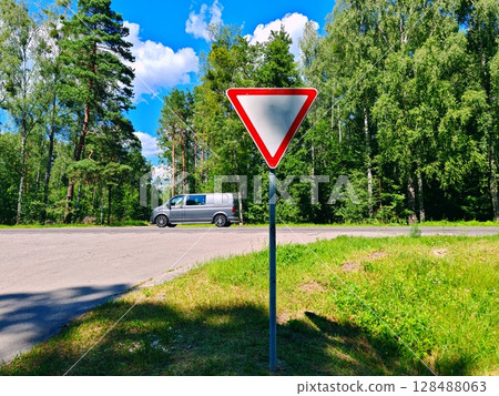 Road sign "give way" on the background of green. Road sign, secondary road on a country highway Road sign "give way" on the background of green. Road sign, secondary road on a country highway 128488063