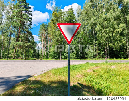 Road sign "give way" on the background of green. Road sign, secondary road on a country highway Road sign "give way" on the background of green. Road sign, secondary road on a country highway 128488064
