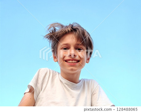Closeup portrait of smiling school boy looking at camera. portrait of a happy Caucasian teenager boy against a blue sky 128488065