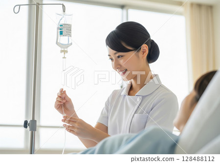 A Japanese female nurse in a white coat giving an IV to a patient 128488112