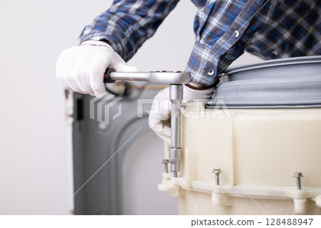 Washing machine repair. Professional service worker fastening bolts on washer tub drum after changing broken malfunction parts 128488947