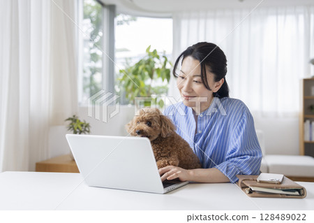 Middle-aged woman working on a computer and her pet dog. Image of working from home. 128489022