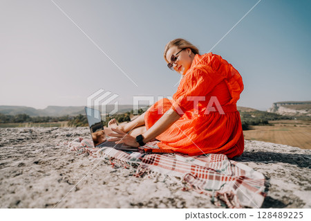 Woman in Orange Dress Working on Laptop on a Mountain Top 128489225