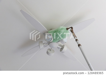 Cleaning the ceiling fan light with a duster Cleaning the ceiling fan light with a duster 128489365