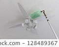 Cleaning the ceiling fan light with a duster 128489367