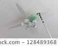 Cleaning the ceiling fan light with a duster 128489368