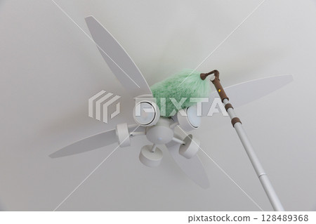 Cleaning the ceiling fan light with a duster 128489368