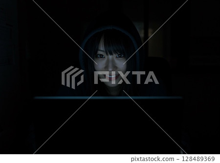A woman in a dark room sits at a computer and posts fake information on social media 128489369