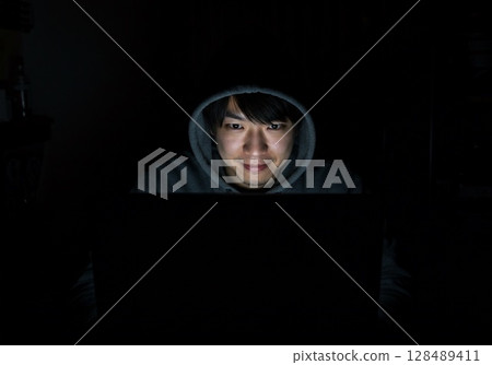 A man sits at a computer in a dark room and posts fake information on social media 128489411