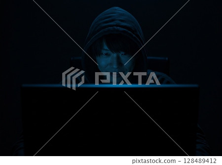 A man sits at a computer in a dark room and posts fake information on social media 128489412