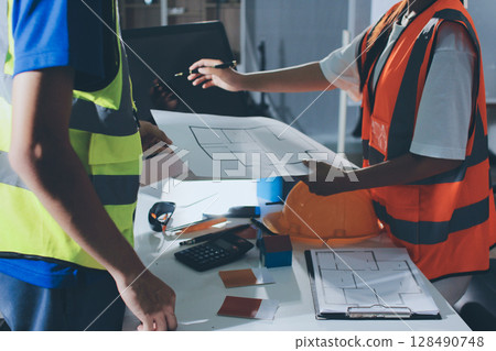 Closeup of team of industrial engineers meeting analyze machinery blueprints consult project on table in manufacturing factory. Working in manufacturing plant or production plant. 128490748