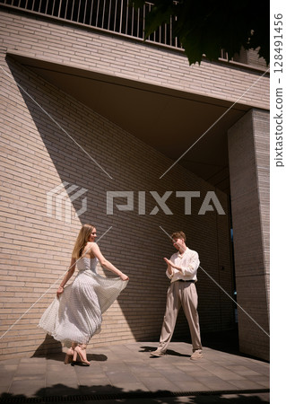 Slow living and mindful lifestyle. Couple dancing elegantly in sunlit modern urban architectured corner Slow living and mindful lifestyle. Couple dancing elegantly in sunlit modern urban architectured corner 128491456
