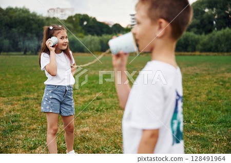 Talking by using string can phone. Boy and girl are together having fun on the field at daytime 128491964