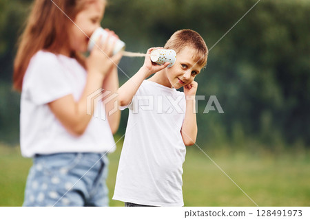 String can phone in hands, talking. Boy and girl are together having fun on the field at daytime 128491973