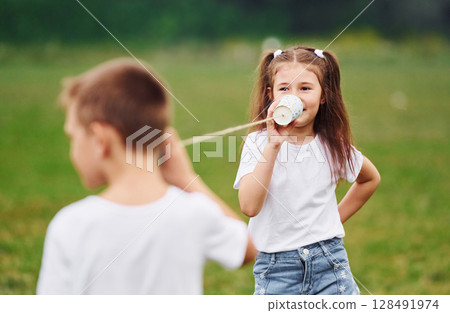 String can phone in hands, talking. Boy and girl are together having fun on the field at daytime 128491974