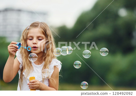 Portrait of little girl that is playing with bubbles outdoors 128492092
