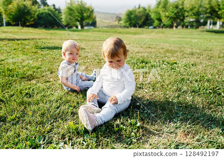 Two kids are sitting on the green field together Two kids are sitting on the green field together 128492197