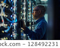 Technician examines complex data server systems in a dimly lit. 128492231