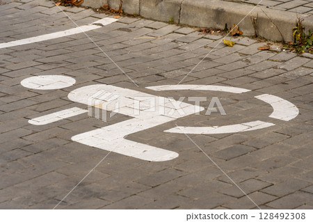 A parking space for individuals with disabilities features a clear symbol on the ground, located on a cobblestone street 128492308