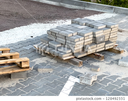 Concrete bricks are neatly stacked on a wooden pallet at a construction site during early morning hours, ready for use 128492331