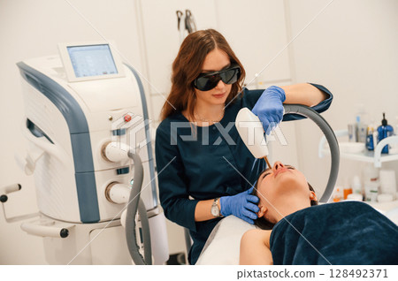 Lying down. Getting photo rejuvenation procedure at cosmetology clinic Lying down. Getting photo rejuvenation procedure at cosmetology clinic 128492371
