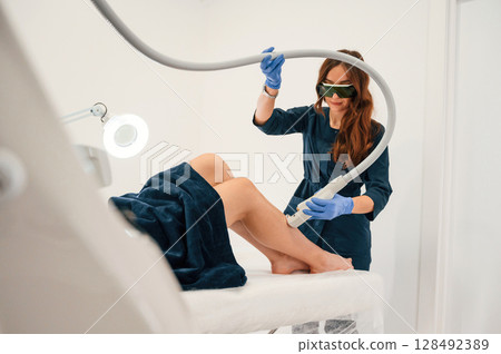 Procedure on the legs. Getting photo rejuvenation at cosmetology clinic. Women in beauty salon Procedure on the legs. Getting photo rejuvenation at cosmetology clinic. Women in beauty salon 128492389