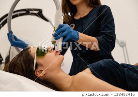 In green protective eyewear. Getting photo rejuvenation procedure at cosmetology clinic. Women in beauty salon 128492416