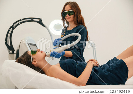 Professional occupation. Getting photo rejuvenation procedure at cosmetology clinic. Women in beauty salon Professional occupation. Getting photo rejuvenation procedure at cosmetology clinic. Women in beauty salon 128492419