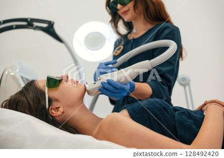 Professional occupation. Getting photo rejuvenation procedure at cosmetology clinic. Women in beauty salon 128492420