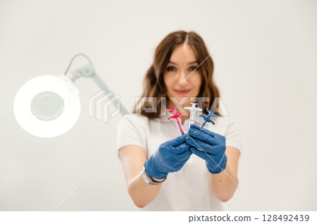 White wall. Cosmetologist holding syringes for injection lips augmentation. Women's cosmetology in the beauty salon 128492439