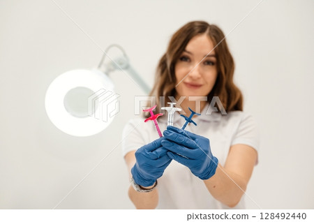 White wall. Cosmetologist holding syringes for injection lips augmentation. Women's cosmetology in the beauty salon White wall. Cosmetologist holding syringes for injection lips augmentation. Women's cosmetology in the beauty salon 128492440